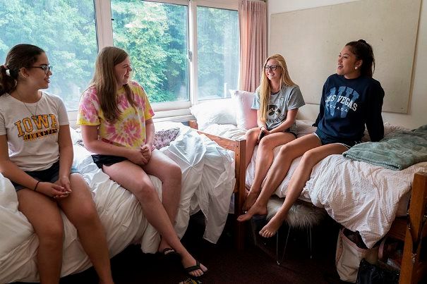 Four girls in shorts and t-shirts sitting on beds in a college dorm room 